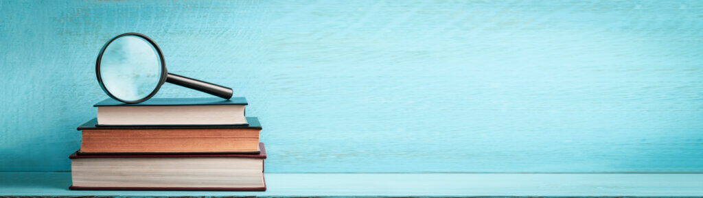 Magnifying glass on stacked books, blue background.