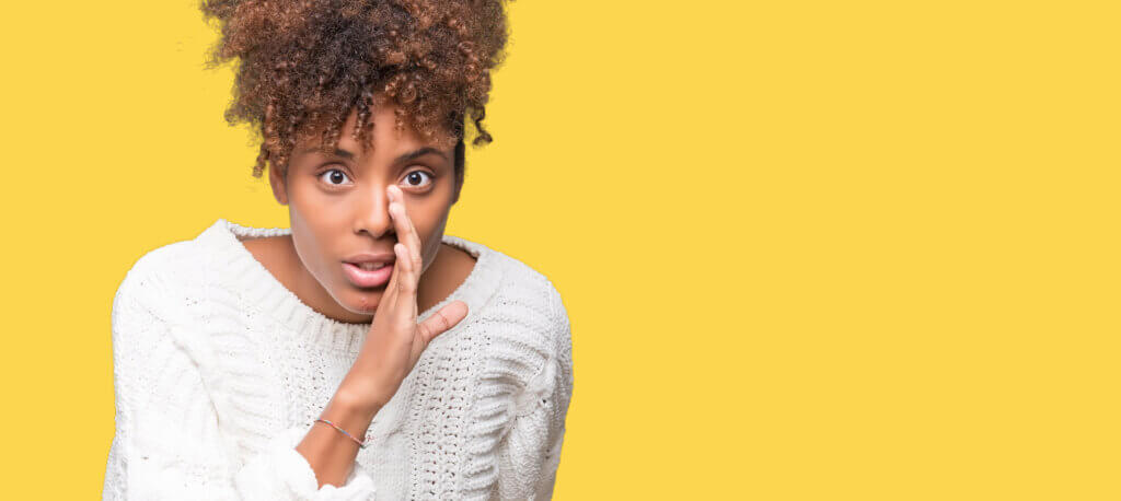 Woman whispering with surprised expression, yellow background.